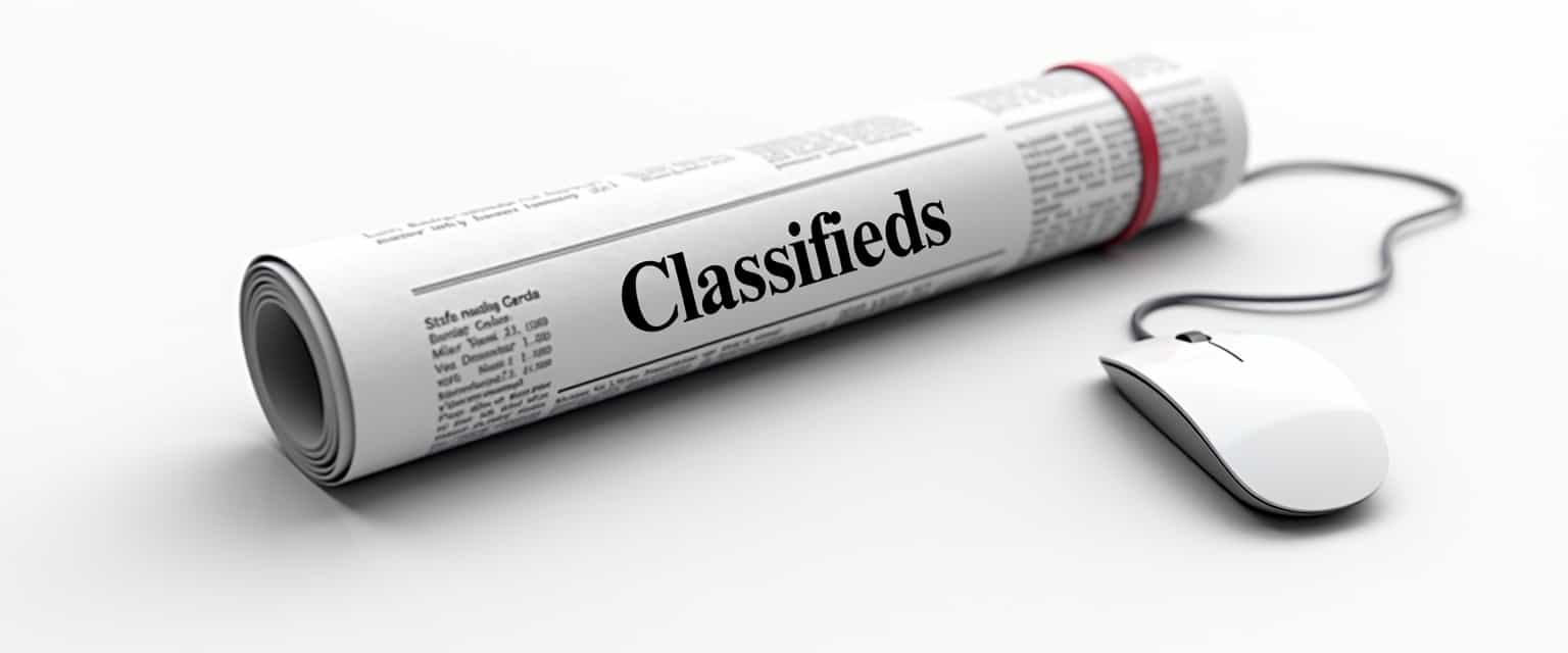 This image depicts a rolled newspaper:2.3 with the word Classifieds prominently displayed across the top. The newspaper is bound with a red rubber band, and its positioned on a white surface, which gives the impression of a clean, uncluttered environment. The newspaper appears to be a standard broadsheet size, and the text is in a bold, black font that stands out against the white background of the paper. The red rubber band is a simple yet effective detail that adds a pop of color to the otherwise monochromatic palette of the image.To the right of the newspaper, there is a computer mouse lying flat, with its cord trailing to the left. The mouse is white, which complements the newspaper and the white background, and it has a modern, sleek design with a rounded shape and a scroll wheel. The cord is thin and white, matching the mouse and the overall color scheme of the image.The art style of the image is realistic, with attention to detail in the textures and shadows. The lighting in the image is soft and diffused, casting gentle shadows under the newspaper and mouse, which gives the objects a three-dimensional appearance. The overall effect is a clean, minimalist composition that suggests themes of traditional media meeting digital technology.The medium of the image is photography, as it appears to be a high-quality digital photograph rather than a painting or illustration. The colors are muted, with whites, blacks, and soft reds and grays dominating the palette, creating a professional and straightforward visual language.