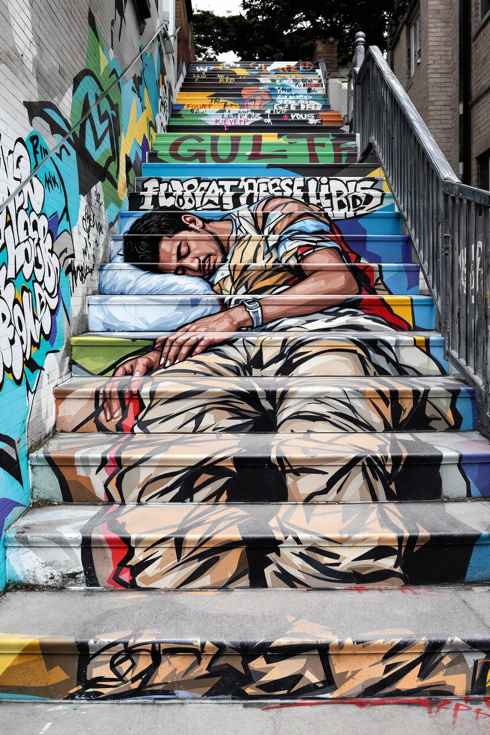 Trompe-l'oeil tegnique, Kevin Lee Art, a vibrant mural painted on outdoor stone steps. The mural features a male person in worn-out, tattered clothing sleeping. The artwork captures themes of hardship and resilience, using bold, contrasting colors and expressive brushstrokes. The stairs are set in an urban environment, with the painting blending into the texture and contours of the stone steps.