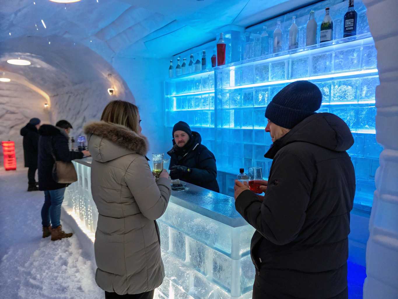 Inside a Bar complete made out of ice in Finnland. Party people in winter dressing enjoy there drinks. Crystal clear atmosphere with transparent ice bar in background illuminated with blue led lighting 