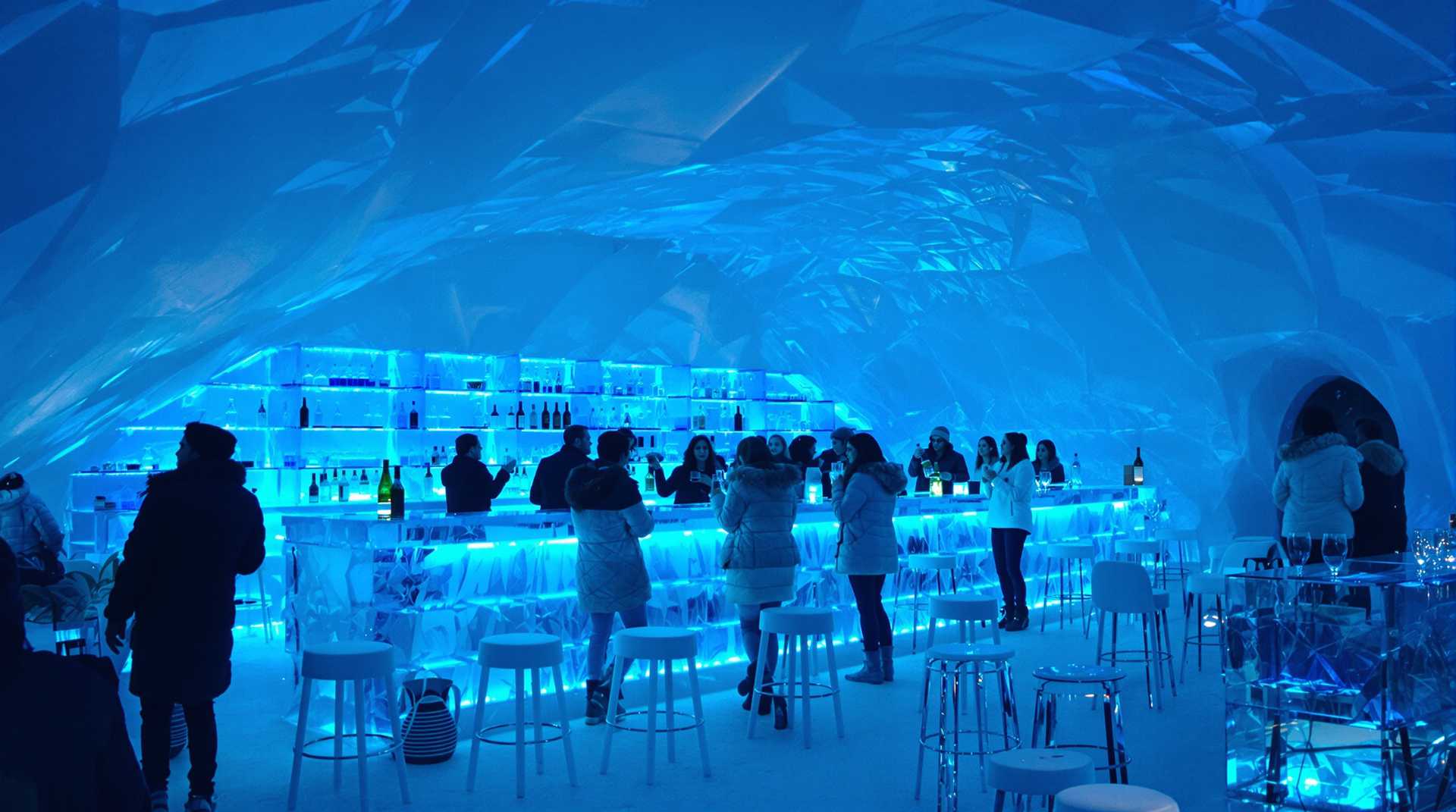 Inside a Bar complete made out of ice in Finnland. Party people in winter dressing enjoy there drinks. Crystal clear atmosphere with transparent ice bar in background illuminated with blue led lighting 