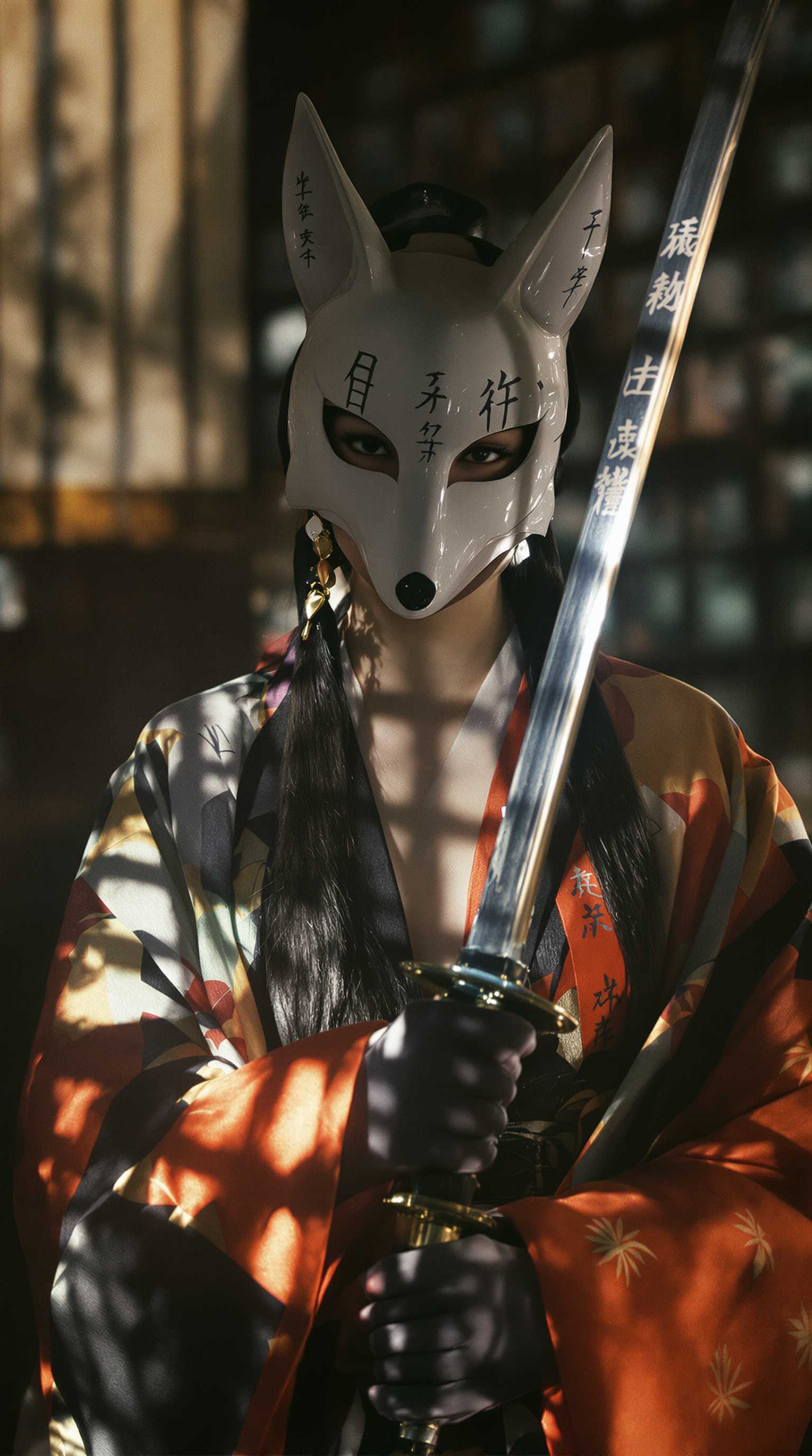 A Japanese culture-inspired scene captured in the emotional style of 35mm film photography. A young Japanese woman stands gracefully, wearing a traditional fox mask that partially conceals her face, creating an air of mystery. She holds a katana with a poised and elegant stance, the blade reflecting soft, ambient light. The scene is enriched by subtle kanji inscriptions either on the katana, her attire, or the background. The lighting plays with reflections, casting a warm and nostalgic glow reminiscent of traditional Japanese aesthetics. The composition exudes an emotional depth, blending cultural symbolism, artistry, and cinematic tones. 