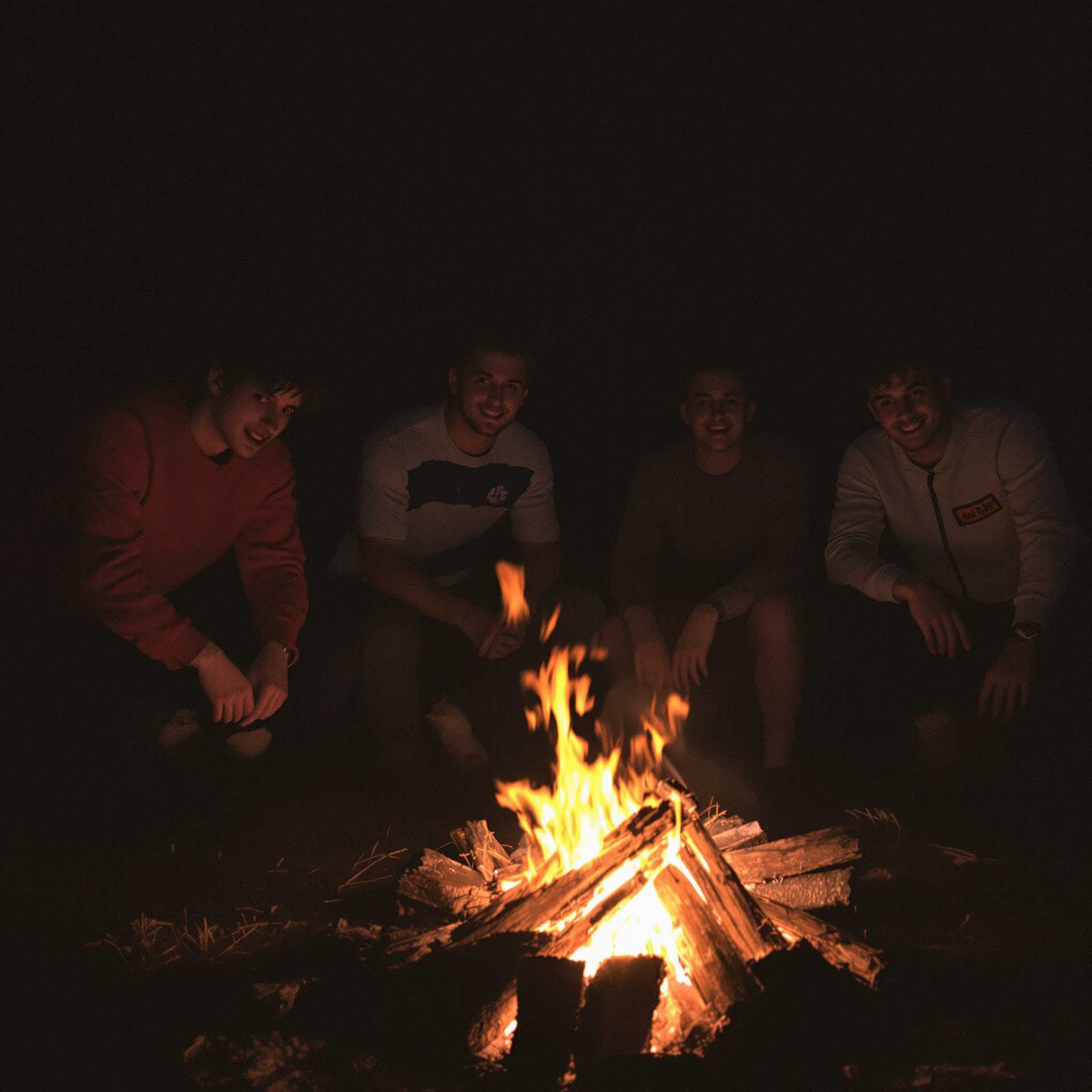 few friends all different style small fire at night in the wood, Slightly grainy image, 1980, Slightly grainy image, 80s outfits, Low key lighting,                                                                                                                                      Fun, drunk, cheer