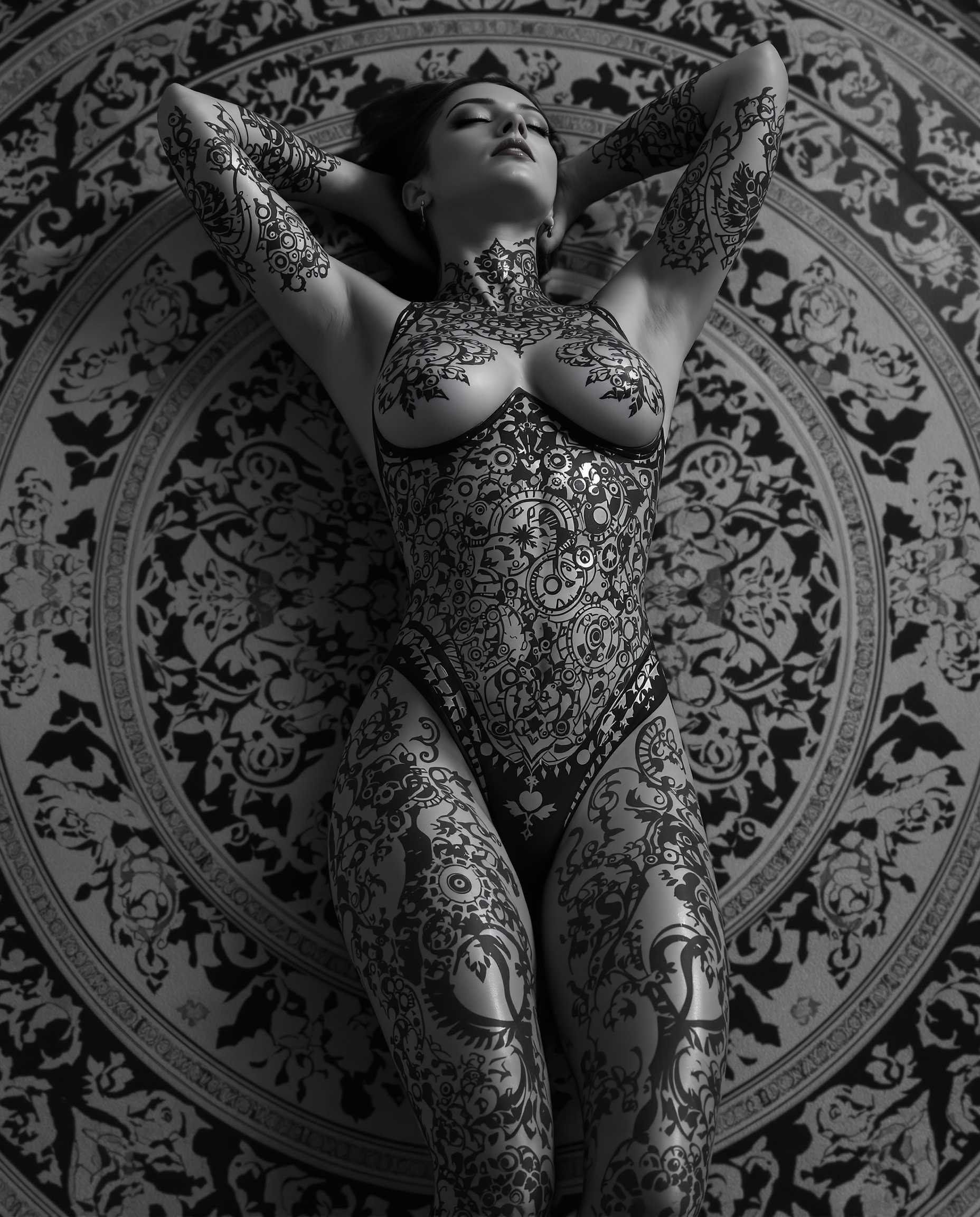 This is a realistic photo (photograph) of a female real person highly stylized and detailed digital artwork, predominantly in grayscale with a few highlights of black and white. The subject of the artwork is a figure lying on their back, with their arms resting behind their head, conveying a relaxed or contemplative pose.The figure is adorned with intricate, gothic inspired tattoos that cover their entire body. The tattoos are elaborate, with a repetitive pattern of circular motifs, floral designs, and what appear to be mechanical elements, such as gears and cogs. The tattoos are executed with precision, and the shading and highlights give them a threedimensional quality.The figure is wearing a formfitting bodysuit that complements the tattoos, with a similar gothic design. The bodysuit is made of a shiny, possibly metallic material, which reflects the light and adds to the threedimensional effect of the artwork.The figure is lying on a circular, ornate carpet or mat that has a complex, symmetrical pattern. The pattern is reminiscent of Islamic or Ottoman style tile work, with interlocking geometric shapes and floral motifs. The carpets design is monochromatic, with shades of black and white, and it provides a stark contrast to the figures tattoos and the shiny texture of the bodysuit.The overall art style of the image is realistic, with a focus on detailed line work and shading that gives the characters and objects a lifelike quality. The medium appears to be digital painting, given the smooth gradients and seamless blending of colors.The colors in the image are primarily shades of gray, with black and white accents. The grayscale palette gives the artwork a moody and atmospheric quality, while the highlights of black and white add depth and contrast.Overall, the image is a striking and visually compelling piece of digital art that combines gothic aesthetics with intricate design and shading techniques.