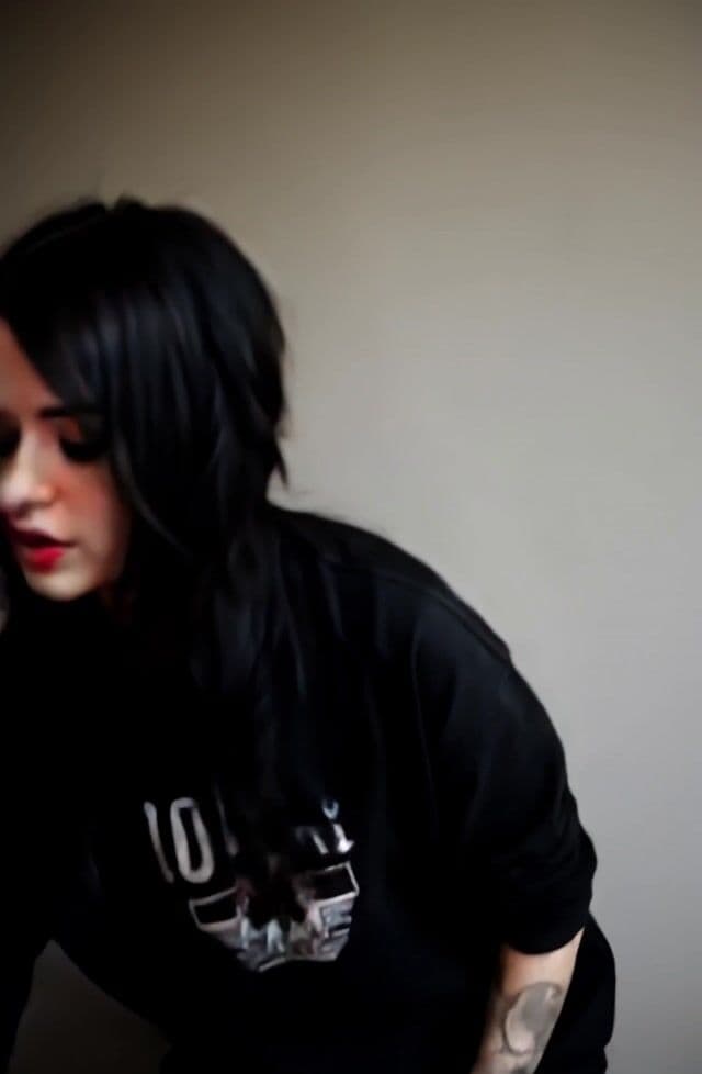 She picks up an acoustic guitar and starts playing and singing while looking at the viewer