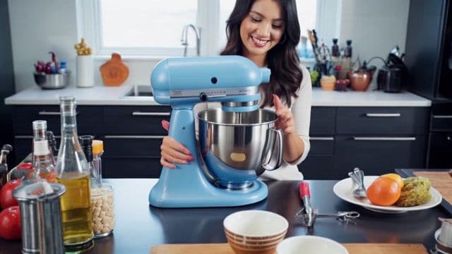 Product review VLOG style video of a woman in a kitchen showing off the features of a blue stand mixer. The woman smiles and talks as she shows off the product to the viewer