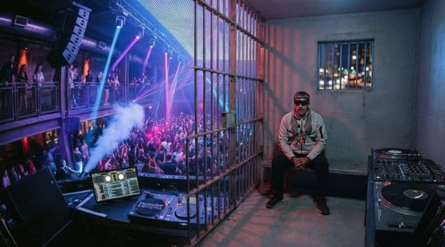 Camera slowly zooms out from maduro as he sits motionless in the jail cell, sighing deeply with no dialog, faint ambient city noises and distant EDM echoes fading out, suggested duration 4 seconds.