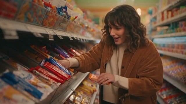 A realistic scene of a woman in a candy store frantically searching to find the last pixel dojo candy bar. once she finds it she exclaims, "gotta have that pixel dojo candy". the candy features a pixelated purple dragon with the text "pixel dojo" on the wrapper.