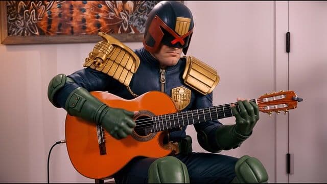 In a warmly lit indoor room with a vibrant orange abstract painting on the wall and a white door framing the background, a stern Judge Dredd in his iconic blue armored suit, gold epaulets gleaming, red visor glowing faintly, sits on a wooden chair cradling a bright orange flamenco guitar with green-gloved hands poised on the strings. He begins passionately playing intricate rasgueado strums and rapid fingerpicking, his armored shoulders subtly swaying in rhythm as the guitar's body vibrates gently, foreground frets blurring with motion while the static background painting and door create depth with parallax shift. The 35mm lens camera steadily dollies in from medium shot to close-up on his hands and visor over 10 seconds, soft diffused indoor lighting casting golden highlights on the gold accents and orange wood, cinematic realism with saturated blues, greens, and oranges evoking gritty noir mood. Crisp flamenco guitar strums echo with percussive taps and resonant chords, ambient room hush underscoring the performance.