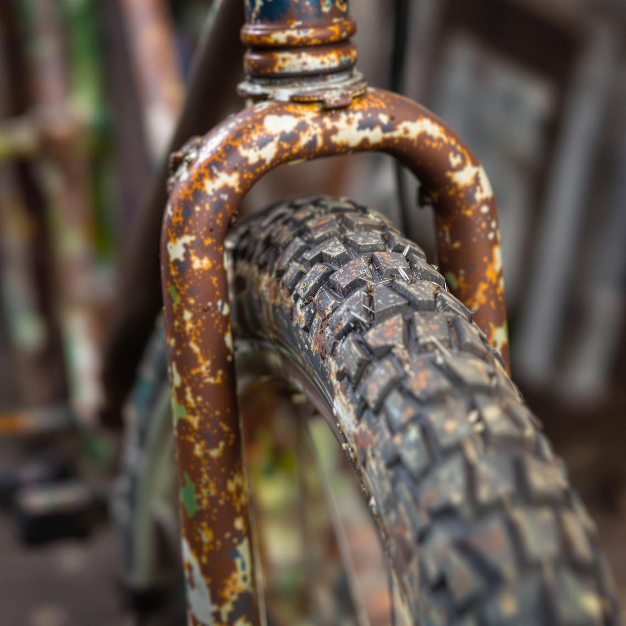 A close-up photograph of a rusty old bicycle with detailed tire treads