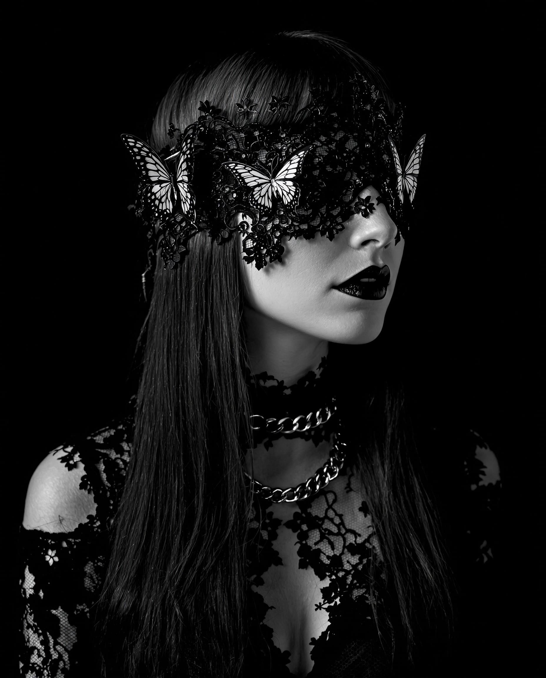 A striking monochromatic photograph of a female figure, captured in a gothic fantasy style with a black-and-white color scheme, emphasizing intricate line work and fine detailing. The subject has long, straight hair cascading down the frame, textured with delicate lacelike patterns, and wears a gothic choker with a chained collar of matching lace design, alongside a black lace blindfold adorned with ethereal butterflies symbolizing transformation. Set against a dark, nondescript background, the image exudes mystery and elegance with cinematic lighting and 8K detail.