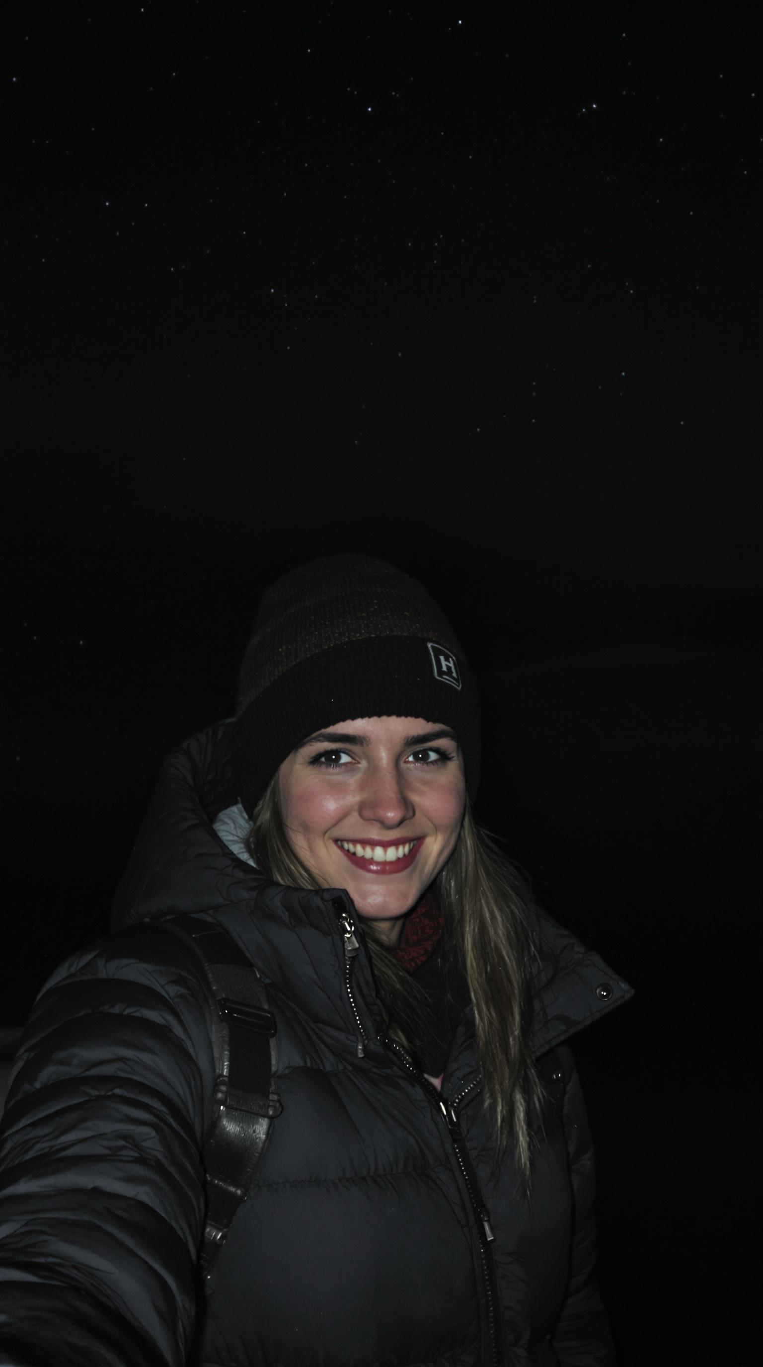 (selfie), young woman on mountains, in the dark, at night, dressed jacket and beanie, Autumn, very dark, grainy, dark moody, (background: stars), solo, Photo realistic, hyper detail, hyper realistic