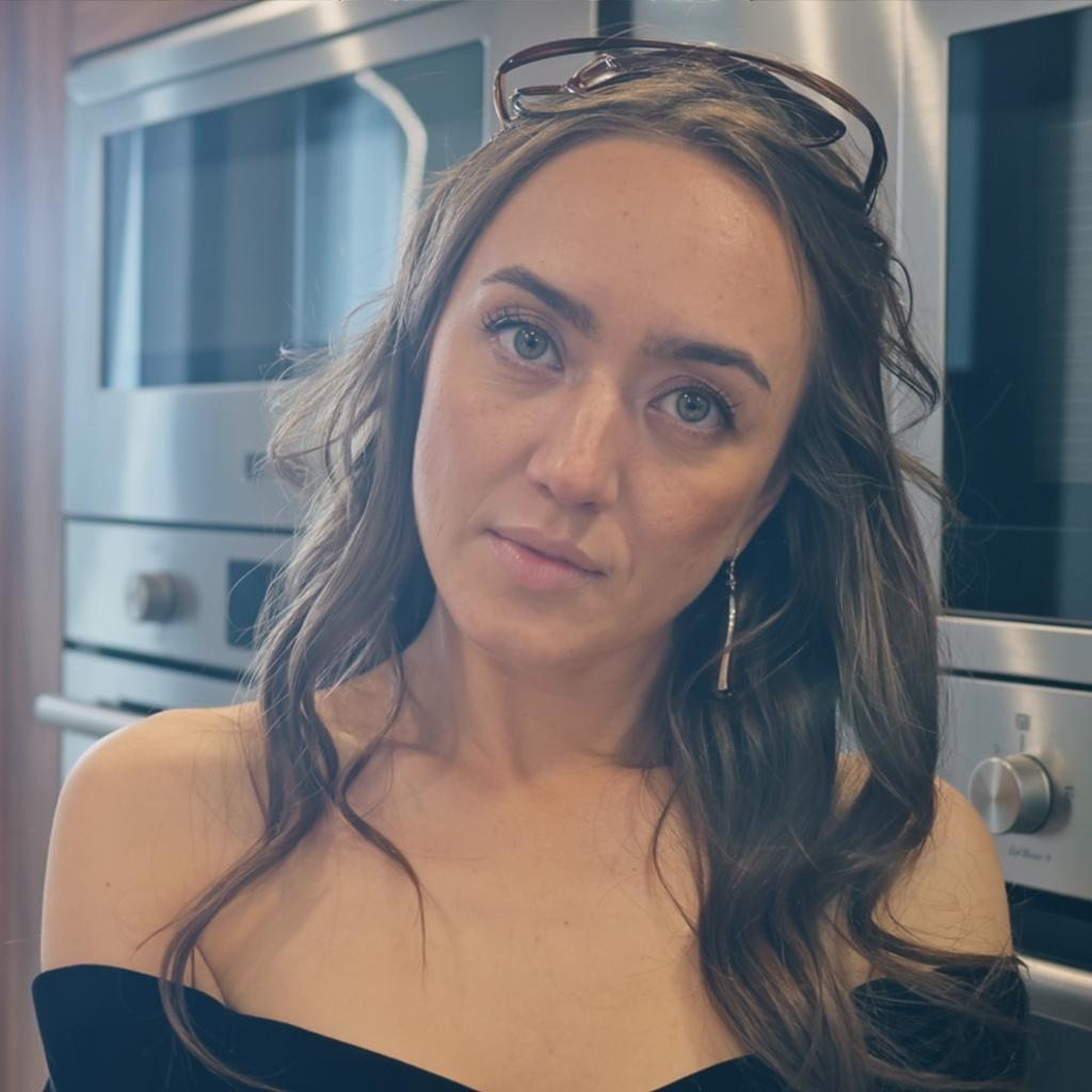 The image is a photorealistic portrait of a stunning woman, characterized by her jet-black hair that cascades elegantly around her shoulders. Her captivating green eyes are framed by long, thick lashes, drawing the viewer's attention and enhancing her enigmatic expression. She wears an elegant black dress that creates a striking contrast against her fair complexion, accentuating her refined elegance. Set in a modern kitchen, the composition features sleek, contemporary appliances and soft, ambient lighting that adds a warm glow to the scene. The kitchen's minimalist design enhances her mysterious and sophisticated aura, while natural light delicately highlights the contours of her face, emphasizing her striking beauty. This compelling and evocative portrait captivates the viewer, merging the elements of fantasy and modernity in a visually stunning way.