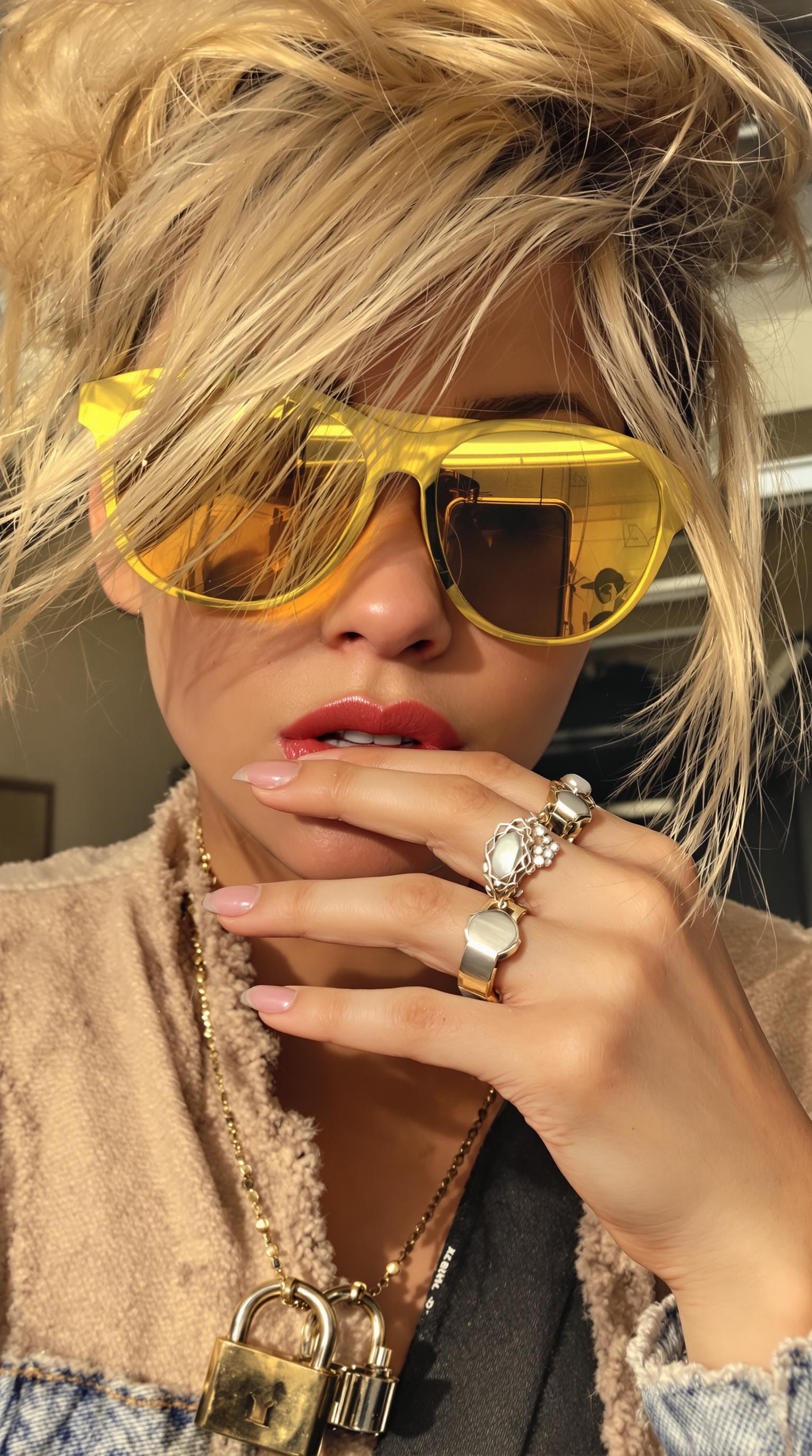 Golden strands rebelliously escape a messy bun as she presses her fingertips stacked with chunky molten silver rings near frosted lips, where subtle gloss barely catches the midday stairwell’s cold fluorescent glow. The yellow-tinted lenses curve around her face, reflecting an iPhone’s faint reflection in neat lock pendant’s shimmer. Tiny skin pores texture the sun-kissed cheek, contrasting with brushed metal ripples blurred softly behind her. Denim cuff fuzz peeks near the wrist, and the frame slants just enough to catch this unstudied moment, where molten silver forms dance in the ornate collage of a modern muse. up captured on Iphone, hand-face jewelry focus