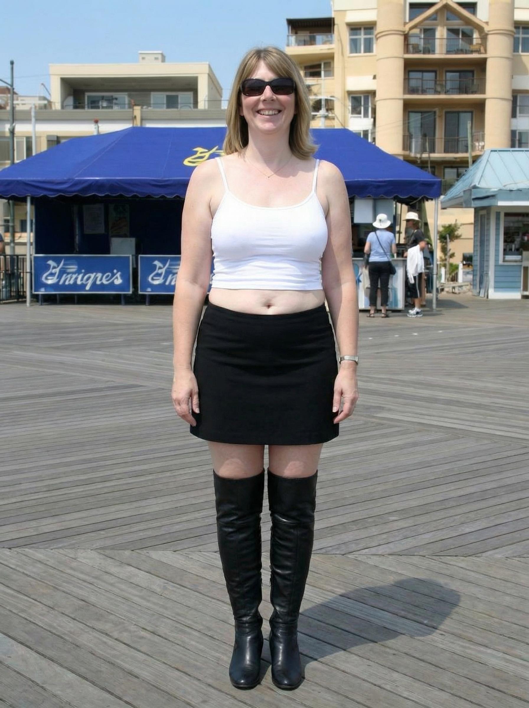 "show me this person standing from the front side wearing a white crop top with very thin straps and no bra under it with larger breasts , showing her slightly soft midriff and a mini black skirt with the sun glasses on and a happy facial expression" "Show me her wearing black thigh high boots" (edited with Google Nano Banana Pro)