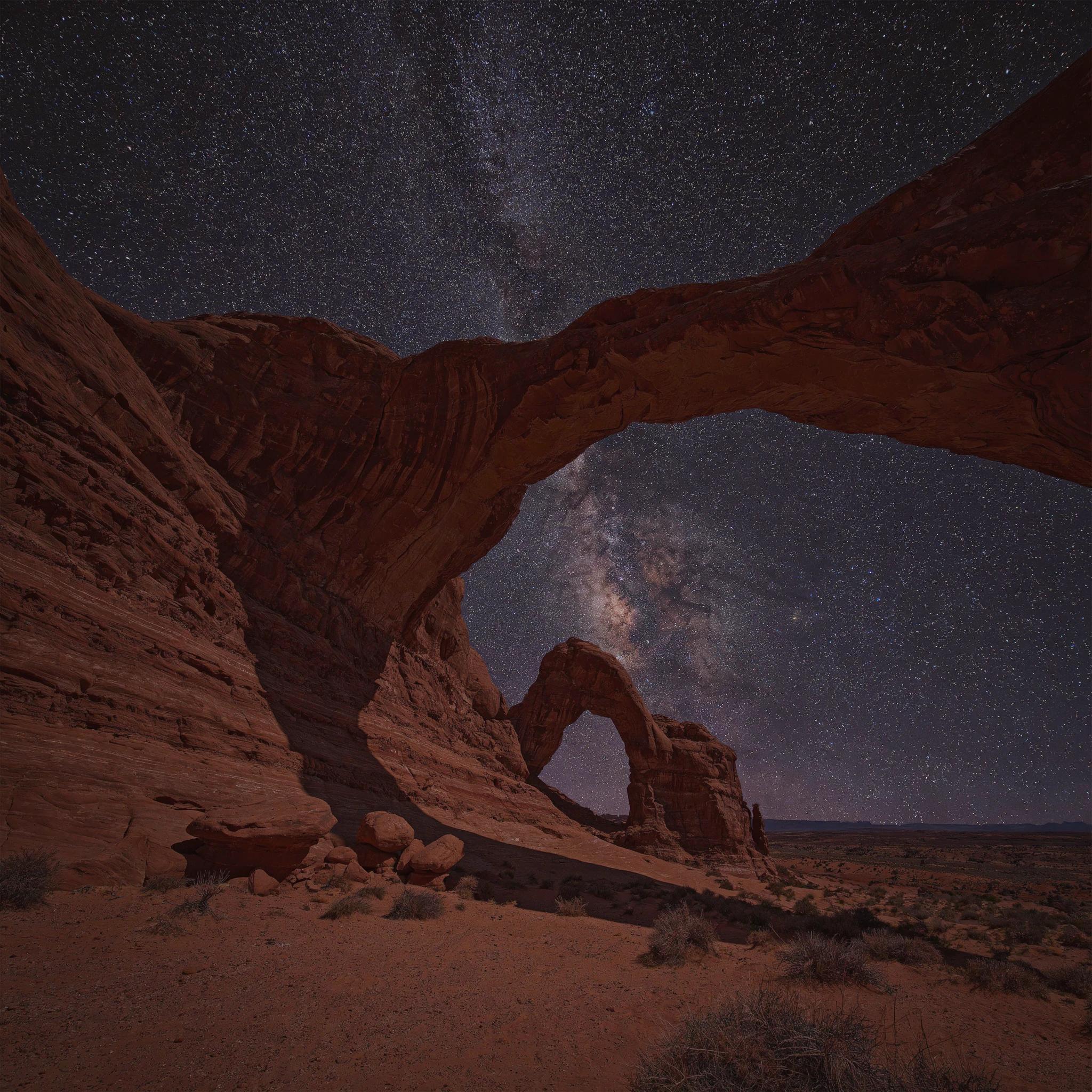 A dramatic desert with towering red rock arches under a starry sky, long exposure
