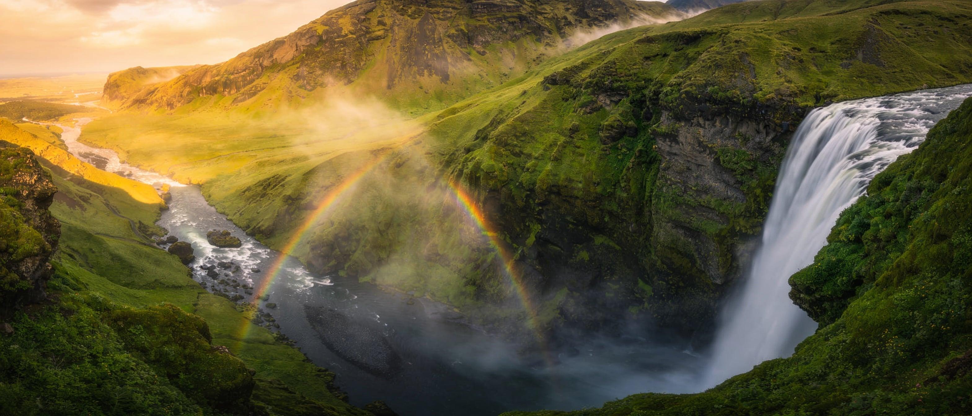A powerful waterfall cascading through a lush green canyon, mist catching rainbow light, wide landscape