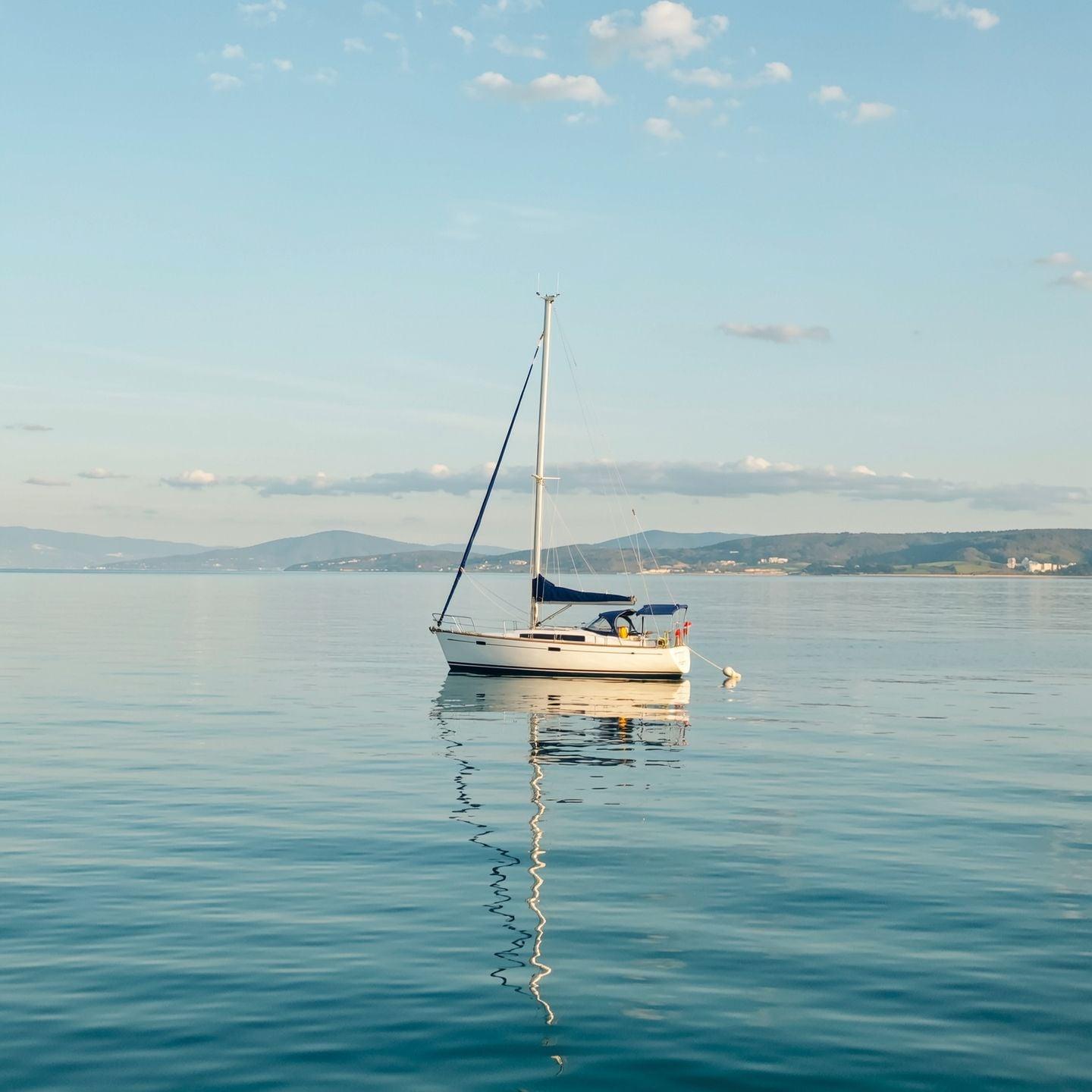 A lone red sailboat on a calm turquoise sea at golden hour, minimalist composition, gentle reflections