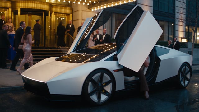 Duke beside the new Tesla Roadster, its door raised, outside a grand hotel at dusk