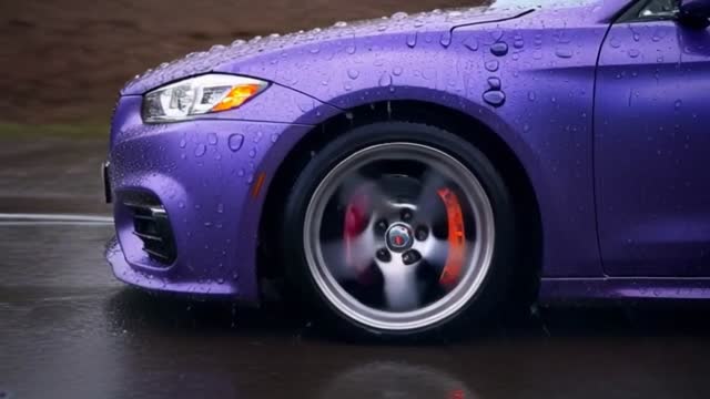 the ultra-wide-angle lens follows closely from the hood, with raindrops continuously splattering
against the lens. Ahead, a sports car speeds around a corner, its tires violently skidding against the wet road,
creating a mist of water. Neon lights refract in the rain, leaving colorful streaks on the car’s surface. The camera
swiftly shifts to the side of the car, capturing the wheels spinning at high speed, before finally moving to the rear