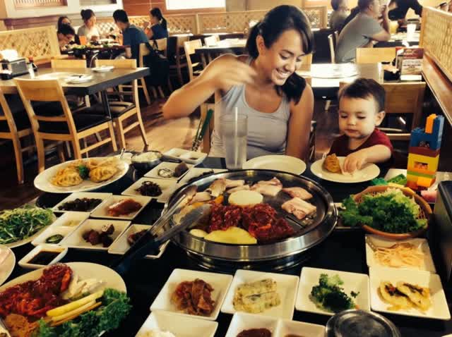 a woman smiles as they eat korean food