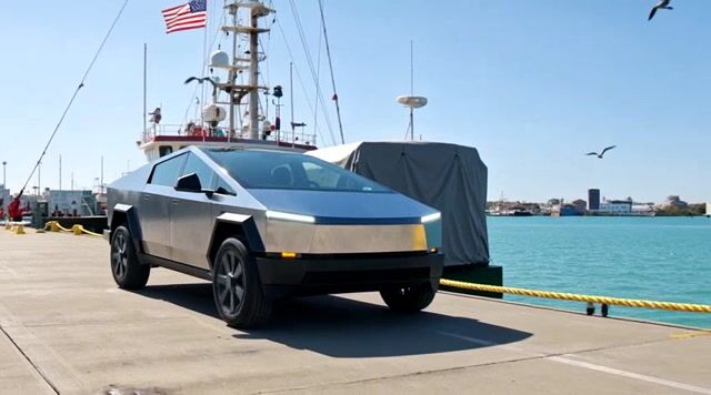 {
  "shot_composition": "A wide-angle three-quarter front view of a sleek blue Tesla Cybertruck parked on a gray concrete dock, facing slightly to the right with its angular futuristic design prominently featured, including sharp lines, black wheels, and illuminated headlights, framed to include the surrounding harbor elements in the background.",
  "scene_setting": "A bright sunny harbor dock area with clear blue skies dotted with flying birds, a tall fishing boat mast adorned with an American flag and navigation lights in the background, a covered gray structure resembling a tarped boat nearby, yellow coiled ropes on the ground, calm blue water extending to the horizon, and industrial white buildings along the waterfront under intense daylight illumination.",
  "subject_wardrobe": "",
  "motion_animation": "The blue Tesla Cybertruck begins to move from its parked position on the concrete dock, accelerating slowly and smoothly driving away towards the right side of the frame along the pier, with its wheels rotating gently and body gliding forward at a steady, unhurried pace over the textured ground.",
  "camera_movement": "",
  "visual_style": "Realistic high-resolution photographic style with vibrant blue hues dominating the car and sky, sharp details on metallic surfaces, bright natural sunlight creating subtle shadows and highlights, and a clean modern aesthetic evoking innovation and serenity in a maritime environment."
}