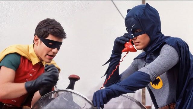 Opening shot: Medium interior shot of Batman and Robin seated in the Batmobile cockpit, Batman holding a red phone to his ear with Robin watching intently, captured with a 35mm lens for balanced framing.
Camera movement: Slow push-in from medium to close-up on Batman's face, building tension at a measured pace over 5 seconds.
Subject and action: Batman receives an incoming call on the red Batphone, lifting it to his ear with a serious expression as he listens to Catwoman's voice, while Robin leans in curiously, gripping the dashboard.
Motion cues: Subtle parallax as the dashboard elements shift slightly against the hazy background; foreground phone cord occludes part of Batman's glove, emphasizing cockpit depth.
Scene setting: Confined Batmobile interior with metallic controls and windshield, set in a foggy outdoor environment during daytime with diffused natural light.
Aesthetic and grade: Retro 1960s comic-book style with vibrant primary colors, slight film grain and warm saturation for a campy, nostalgic TV show feel.