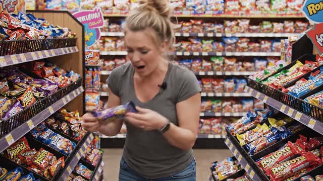 A realistic scene of a woman in a candy store frantically searching to find the last pixel dojo candy bar. once she finds it she exclaims, "gotta have that pixel dojo candy". the candy features a pixelated purple dragon with the text "pixel dojo" on the wrapper.