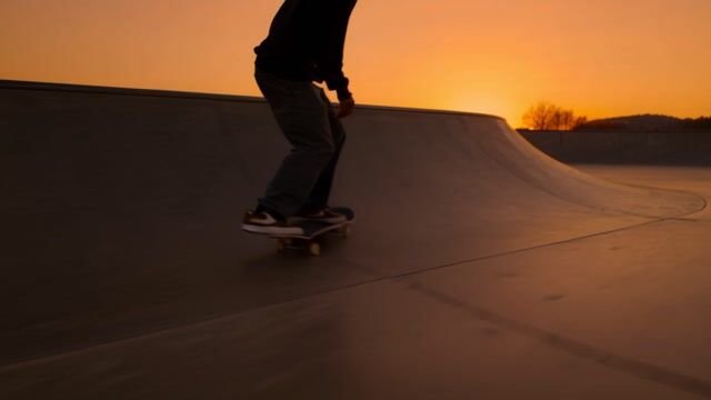 a skateboarder carving through an empty concrete skatepark at dusk, dynamic tracking shot, orange sky
