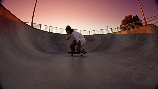 a skateboarder carving through an empty concrete skatepark at dusk, dynamic tracking shot, orange sky