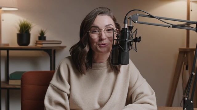 a podcast host speaking warmly into a studio microphone, saying a short welcome, cozy warm lighting, slow camera push-in