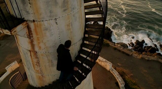A weathered lighthouse keeper climbs a spiral staircase at dawn, waves crashing below, warm lamplight, cinematic