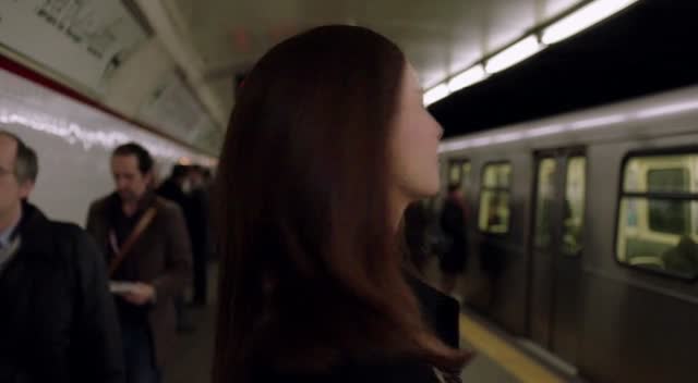 The woman turns and walks away from the camera through a crowded subway station