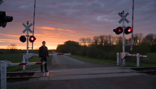 [Image1] defines the logo pattern, energy shapes, and color details. Do not use any background or other elements from the image.

Shot 1: Slow cinematic tracking shot beside an old countryside railway crossing at sunset; the young man in a black jacket stands alone looking down the empty tracks as warning lights begin flashing red, then he raises his head as a gigantic three-headed cobalt blue #1952F0 hydra with glowing [Image1] patterns bursts through distant trees and charges straight toward the crossing; <evening wind, insects, distant birds, sharp DING DING DING railway alarm, heavy THOOM THOOM THOOM footsteps>.

Shot 2: Fast handheld tracking shot as the young man turns and sprints away from the crossing; a speeding freight train rushes in from the opposite direction while the cobalt hydra leaps across the tracks at the last second, its massive tail slamming into a train car and sending sparks and metal debris flying; <loud BWAAAAAAAH train horn, thunderous ROOOAAARRR, KRAAAASH tail impact, SKRRRRRREEECH metal grinding and sparks>.

Shot 3: Medium shot of the man frozen on the ground as a broken train car falls toward him; one hydra head suddenly dives down and catches the wreckage in its jaws inches above his head, then slowly places it aside while the other two heads watch calmly; dust settles as the man looks up and the glowing [Image1] symbol reflects in his eyes; <deep impact rumble fading, soft TINK TINK debris, low protective GRRRRR growl, final cinematic bass hit>.

Cinematic live-action style, rich detail, natural color, dramatic sunset lighting with cobalt blue energy contrast, photorealistic textures. Keep it subtitle-free, avoid generating any text or subtitles. Do not generate a logo. Do not generate a watermark. Throughout the video, characters with completely identical appearance, clothing, and accessories are prohibited. Keep only a single corresponding character in the same frame.