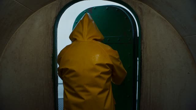 A lighthouse keeper in a yellow raincoat pushes open a heavy door and steps out onto the gallery in wind and rain. A title card reads "CHAPTER ONE" in condensed white all-caps type, centered. Do not misspell it, do not add any other text, do not add subtitles.
