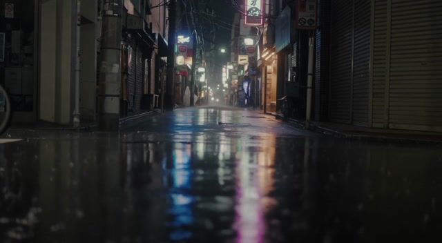 A rain-soaked neon street in Tokyo at night, reflections shimmering on wet asphalt, a lone cyclist passes through frame, soft synth ambience