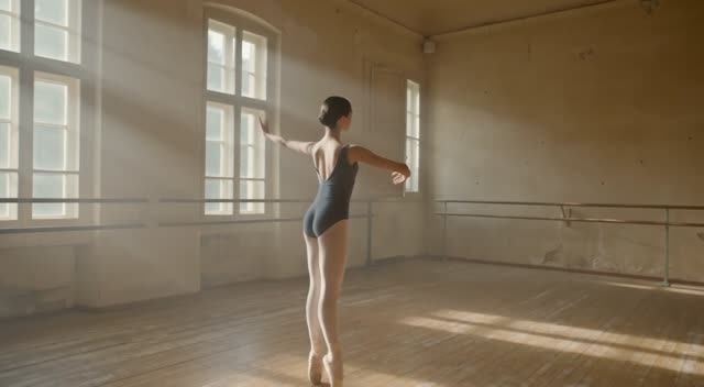 A ballet dancer rehearsing alone in a dusty studio, shafts of window light, slow orbiting camera, piano notes echoing softly