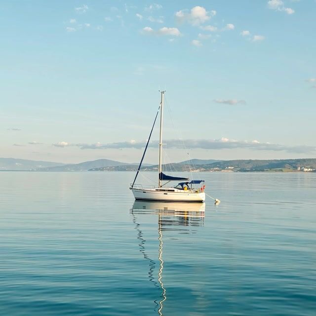 the sailboat rocks gently on the calm sea, sunlight shimmering on the water, slow drifting clouds