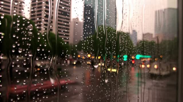 raindrops sliding down a window with a softly blurred city beyond, slow zoom