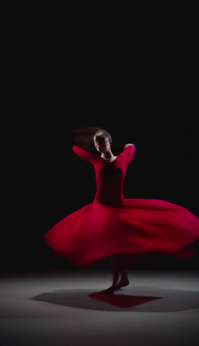 A dancer in a flowing red dress spinning in a dark studio, fabric trailing in slow motion, single dramatic spotlight