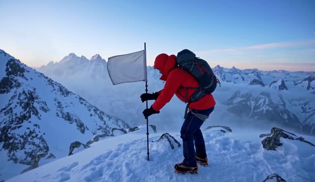 A climber reaches a snowy summit at dawn and plants a small flag, breath visible in the cold. Drone-style pull back revealing the range. Wind and distant echo. No dialogue throughout the entire video.