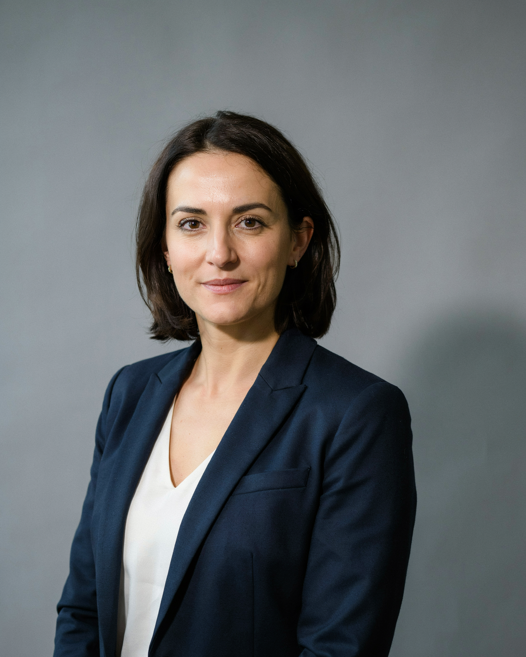 a professional corporate headshot of a woman in a navy blazer, neutral studio background, soft key light, sharp focus