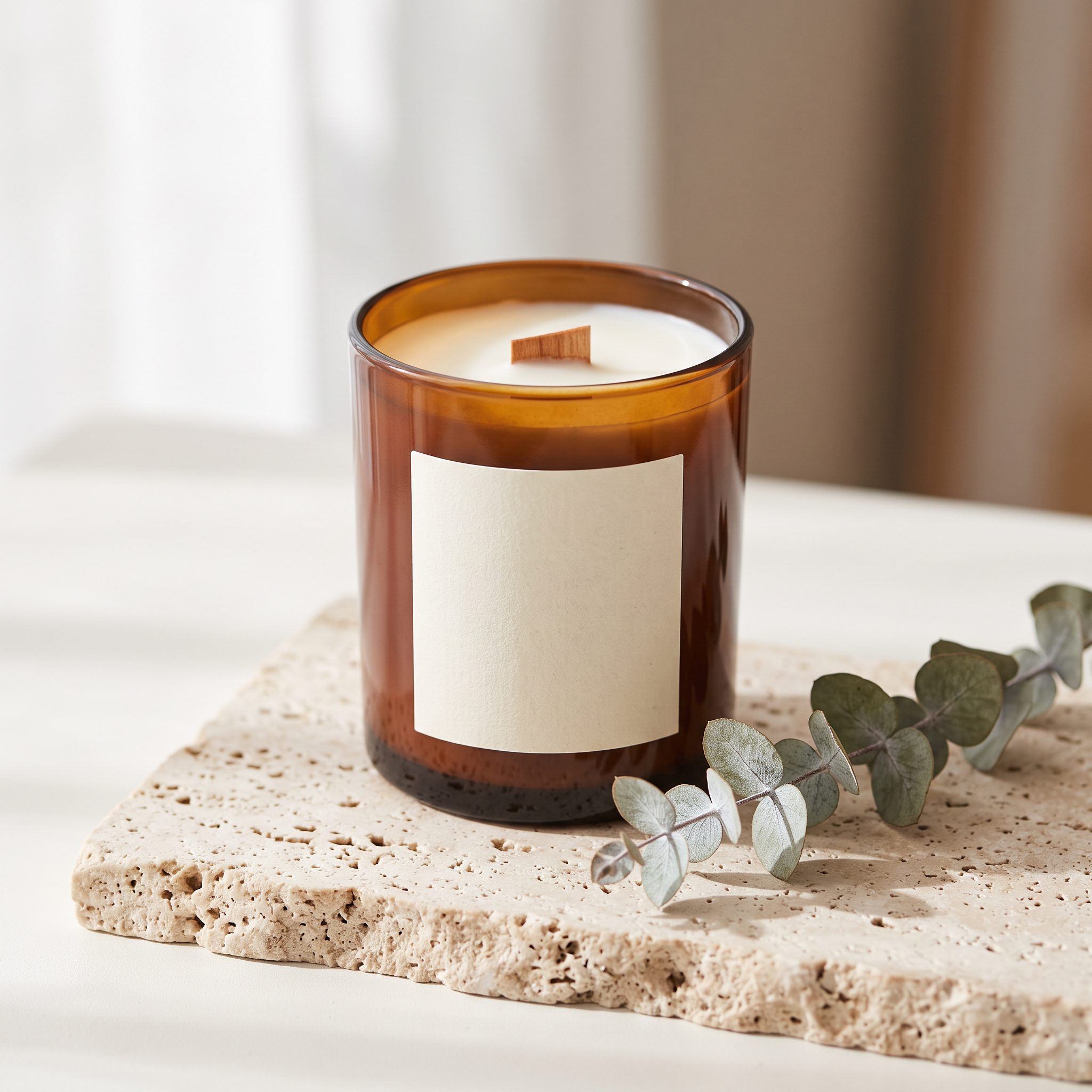 Step 1, the packshot: an amber glass candle with a blank cream label on travertine beside eucalyptus