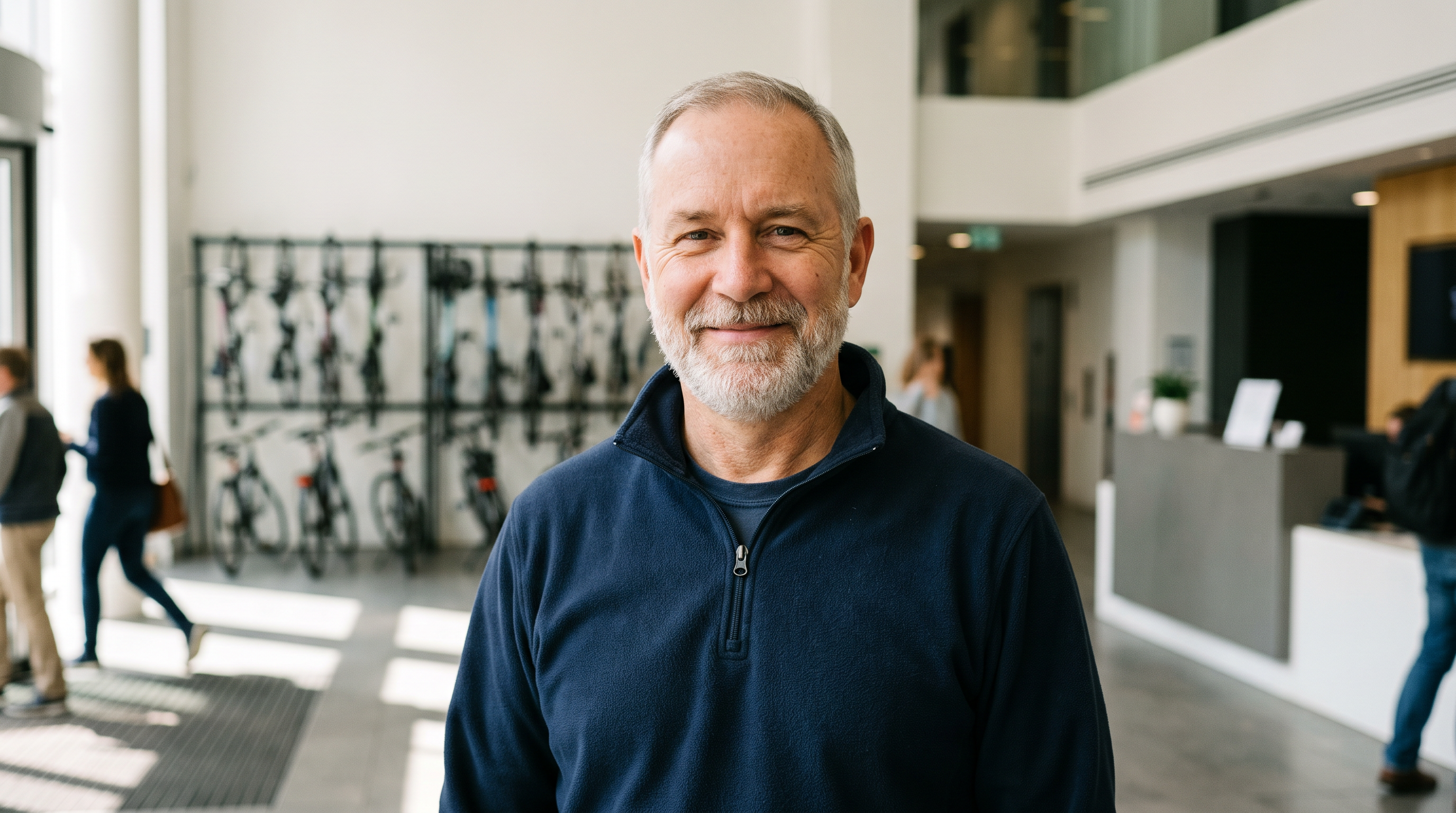 Step 1: a smiling facilities manager in a navy fleece in a bright office lobby with bicycles on a rack behind him