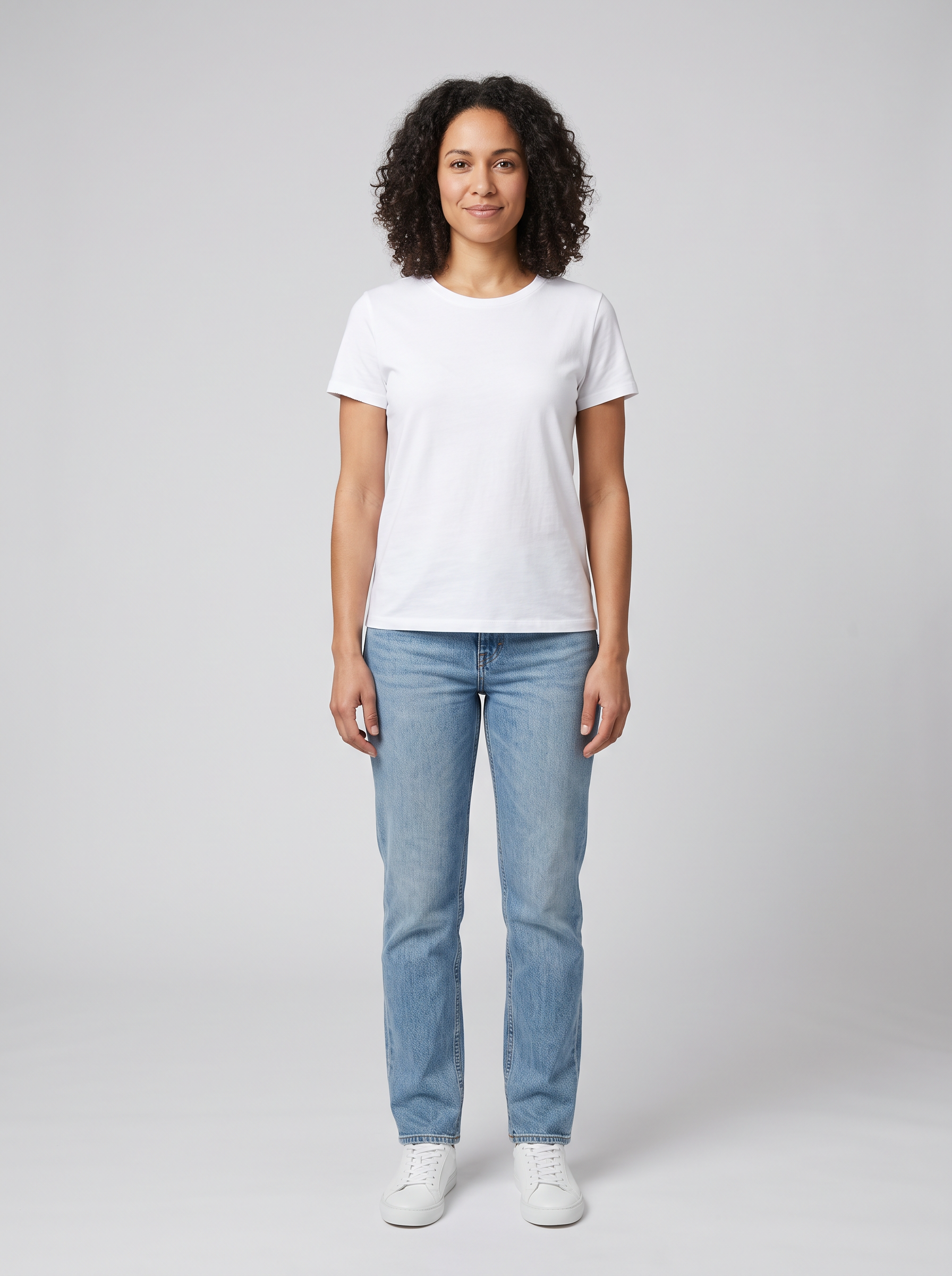 The model: a woman in her thirties with dark curly hair in a white t-shirt, jeans and white sneakers on grey