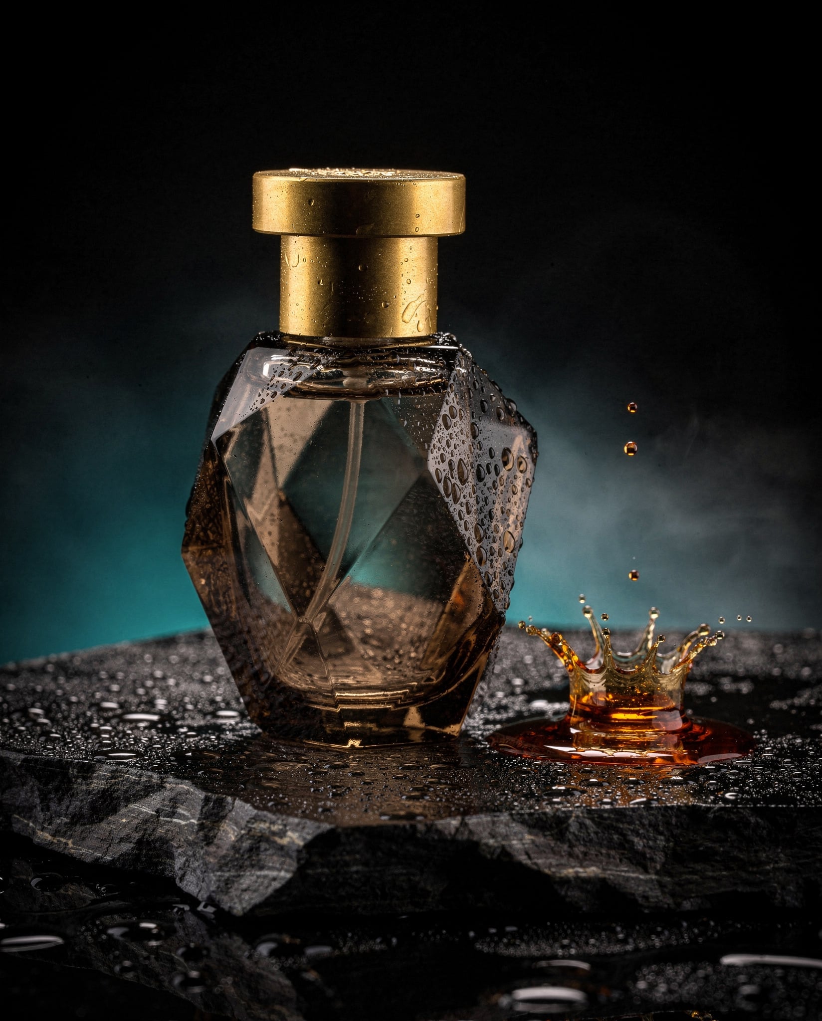 A faceted smoked glass perfume bottle with a brushed brass cap on a wet black basalt slab, beaded with water, while a drop of amber liquid lands beside it in a crown shaped splash against a teal and black background with mist