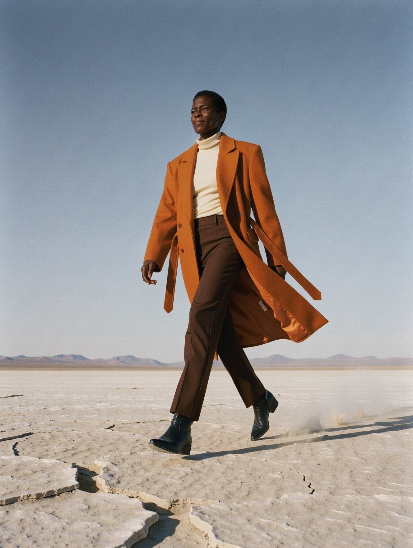 FLUX 3 Image: a low angle full length shot of the woman mid stride in the orange coat, a cream turtleneck and dark trousers