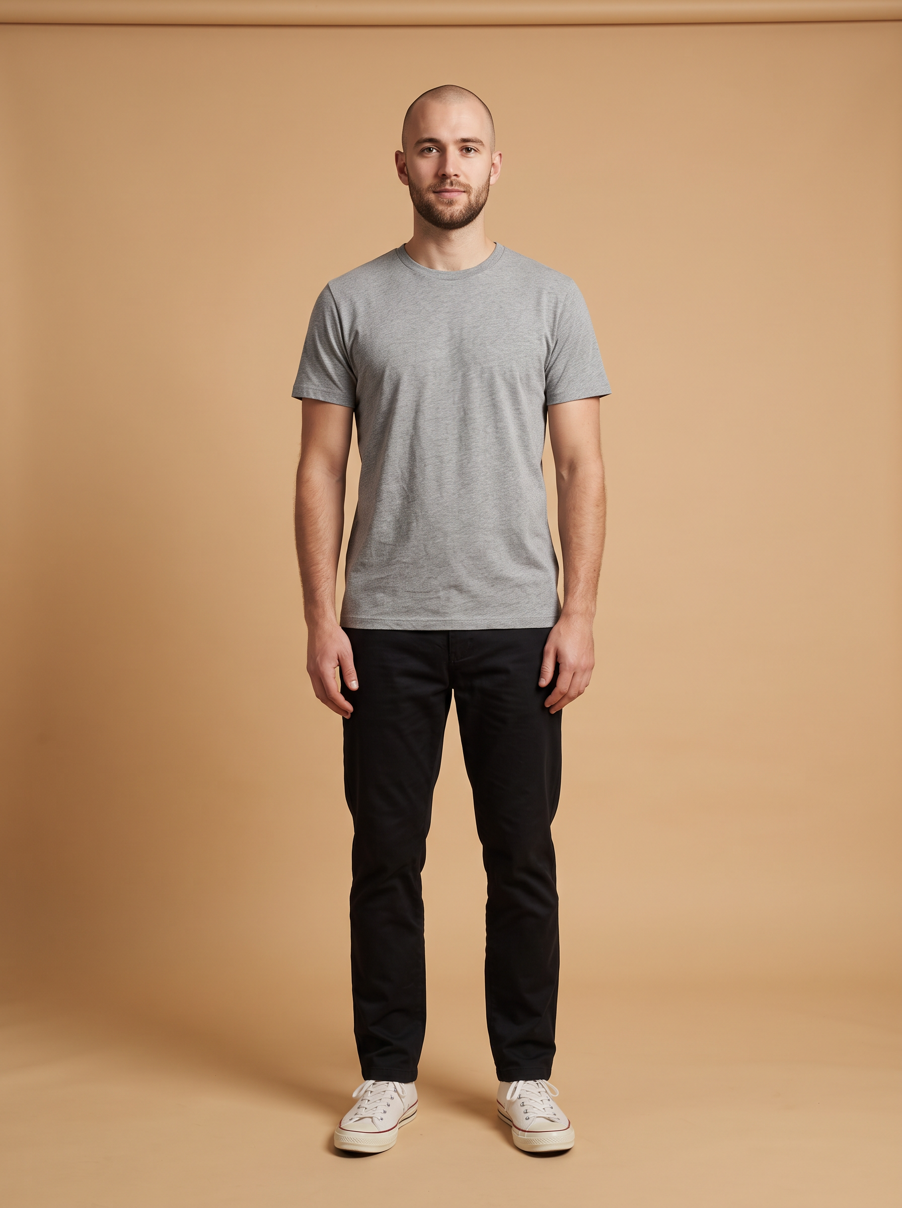 The model photo: a man with a shaved head in a grey t-shirt, black chinos and white sneakers on a beige backdrop