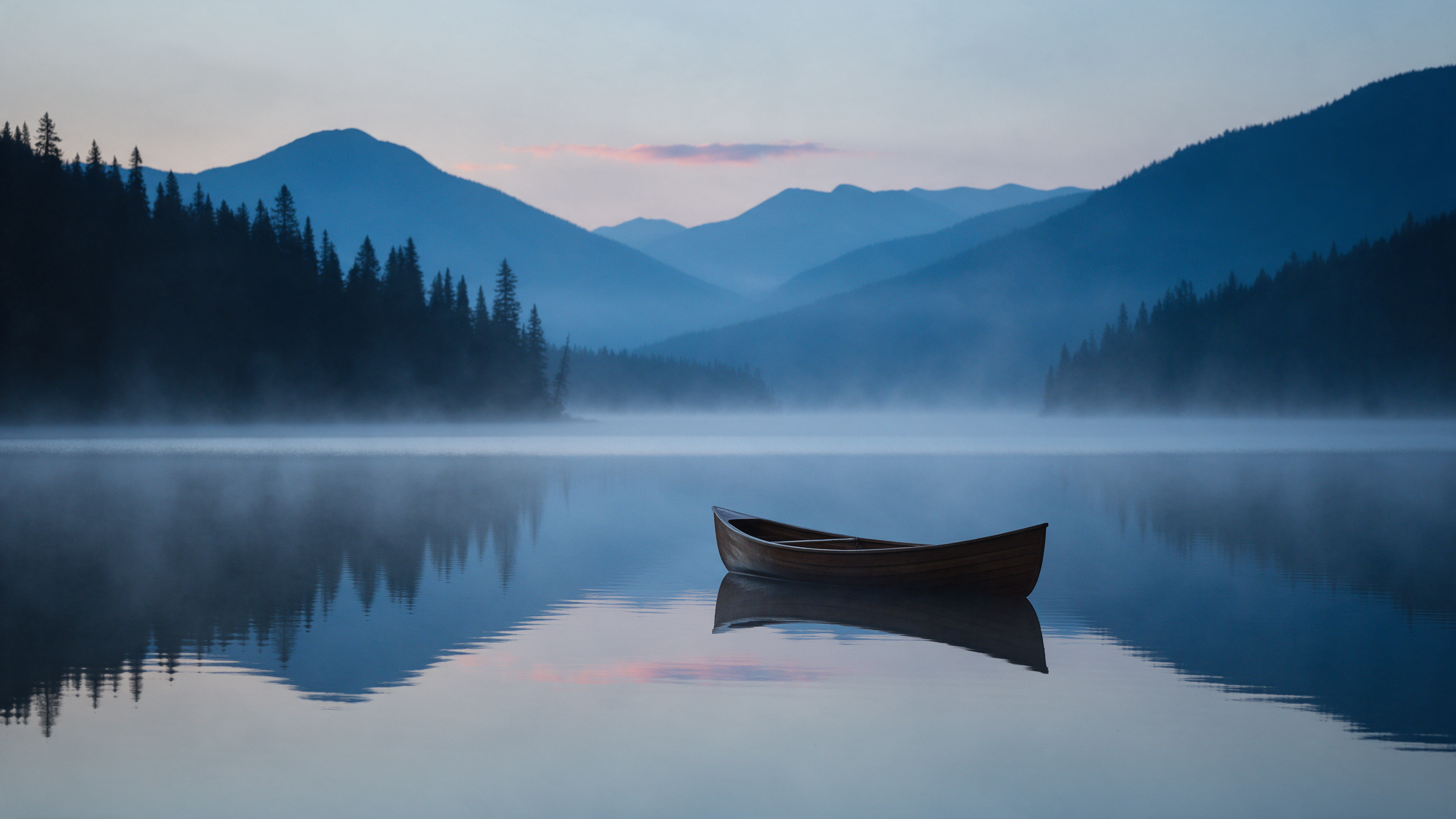 A lone wooden canoe drifts on a mirror calm mountain lake at dusk under layered blue ridges