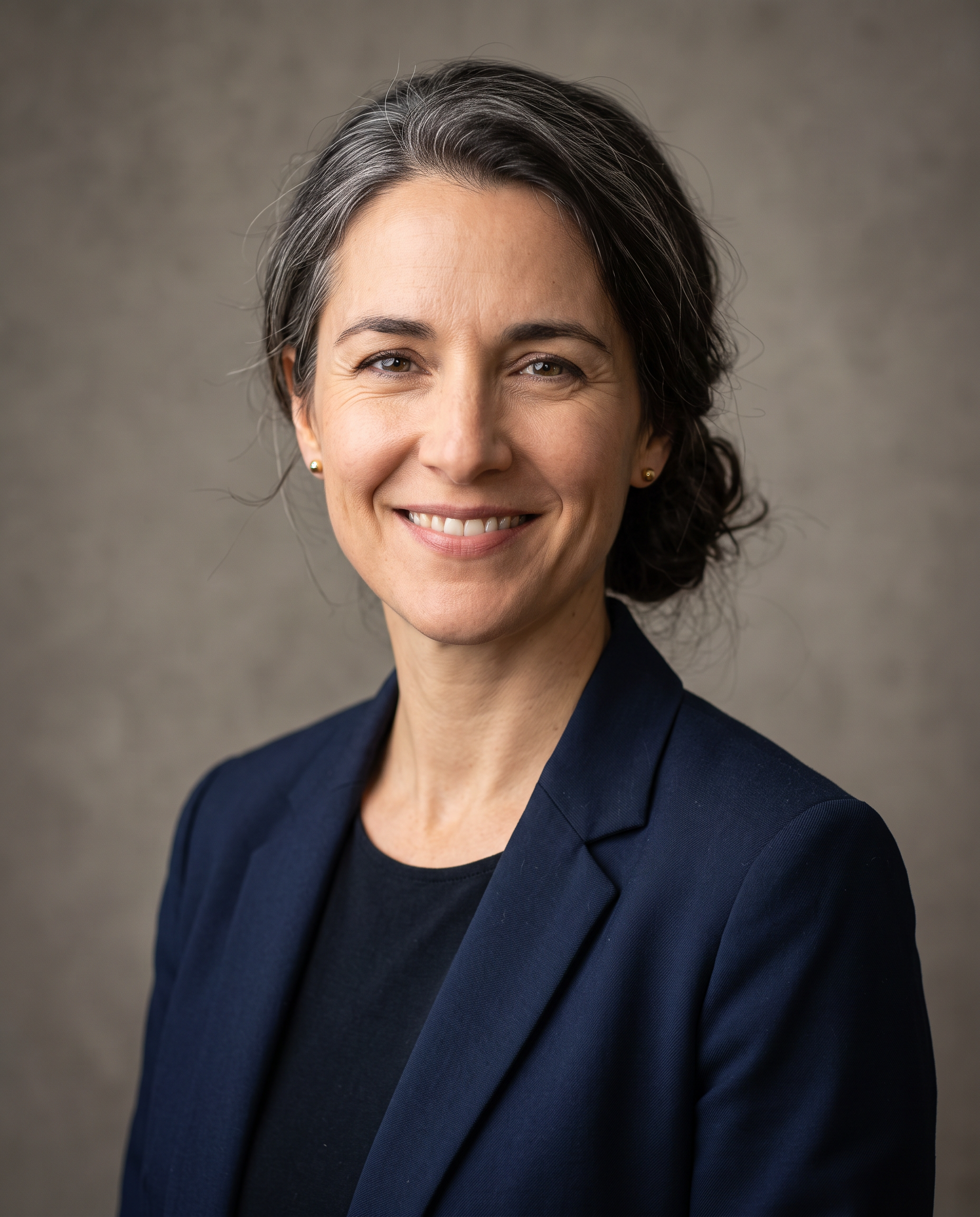 A professional headshot of an architect in her forties with grey streaked hair and a navy blazer