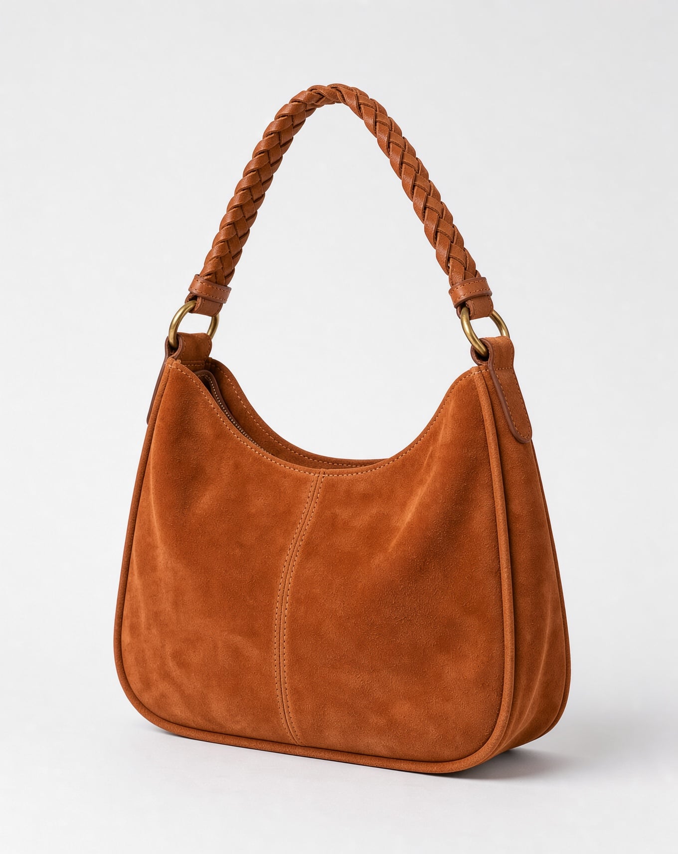 A terracotta suede hobo bag with a braided strap and brass rings on a white background
